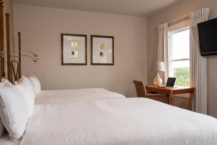 Elegant bedroom with two double beds in white linens, writing desk and chair by a window and artwork on the wall