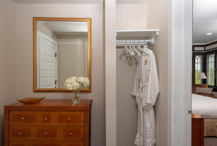 Bedroom with open closet with dresser, gold framed mirror and plush rooe hanging on a white hanger