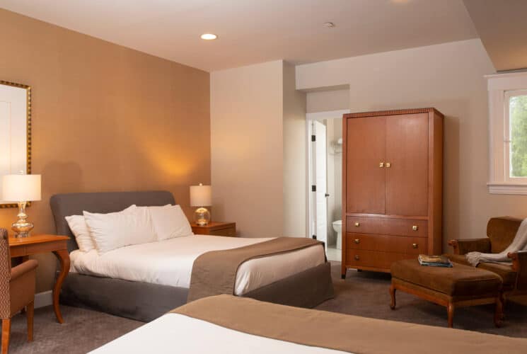 Bedroom with two queen beds, tall armoire , sitting chair with ottoman and writing desk with chair and lamp