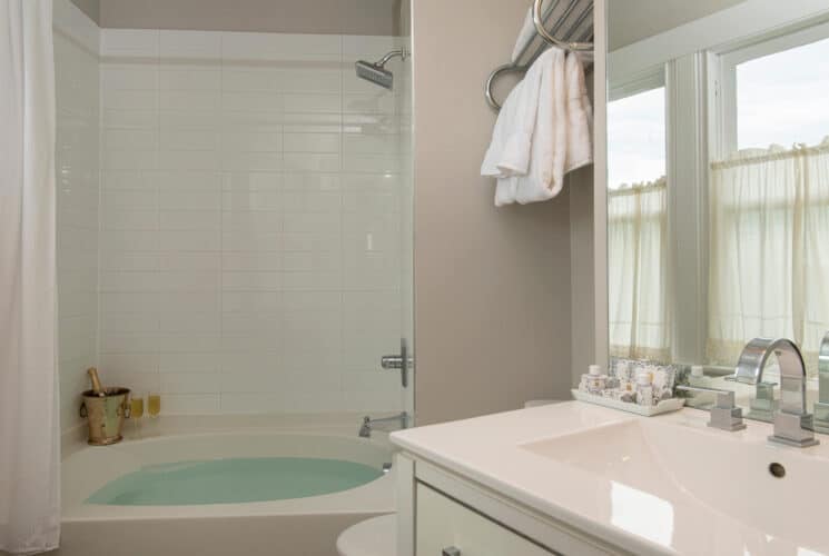 Bathroom with single white sink, shower with soaker tub and white plush folded towels