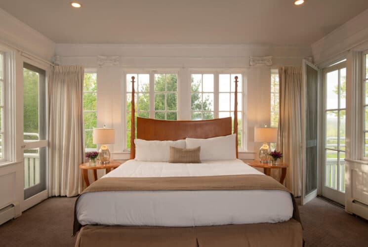 Bedroom with king bed, walls of windows, white curtains and doorway open to an outdoor patio