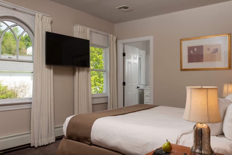 Bedroom with queen bed, large windows with drapes, TV on the wall and doorway open to an attached bathroom