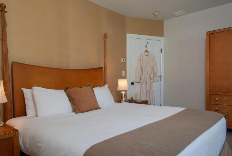 Bedroom with queen bed, white linens, side tables with lamps and plush robe hanging on the door