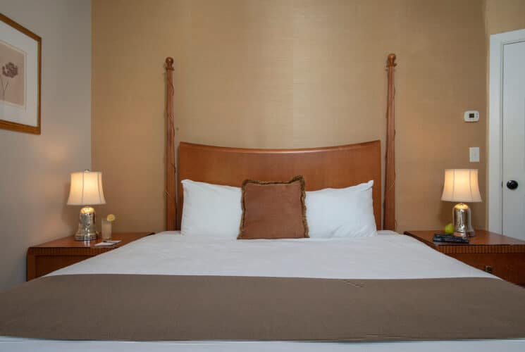 Bedroom with queen bed in white and brown linens, side tables with silver lamps and artwork on the wall