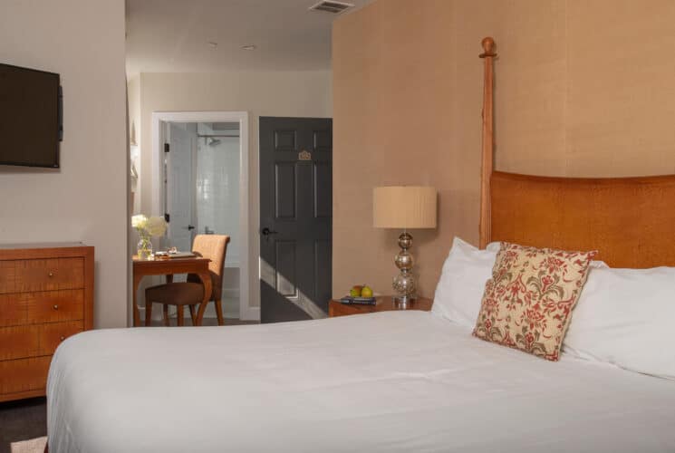 Bedroom with queen bed, dresser with TV above, side table with silver lamp and doorway into adjoining room