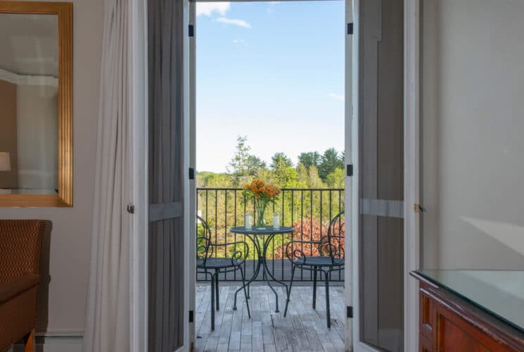 French doors of a bedroom open to an outdoor deck with a patio table and two chairs