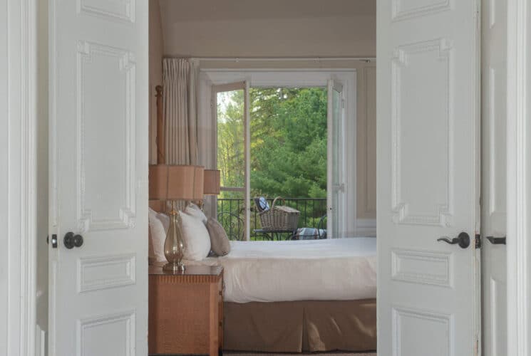 Two doors open to an elegant bedroom with a view of a balcony shown through open French doors