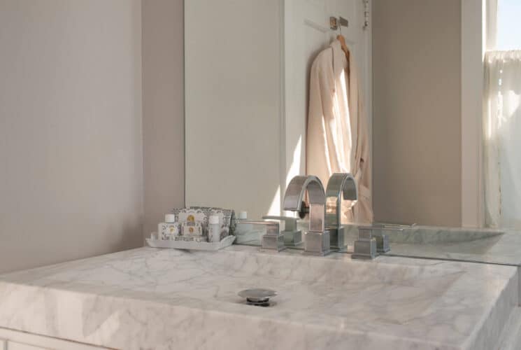 White and grey marble bathroom sink with silver faucet and tray of complimentary toiletries