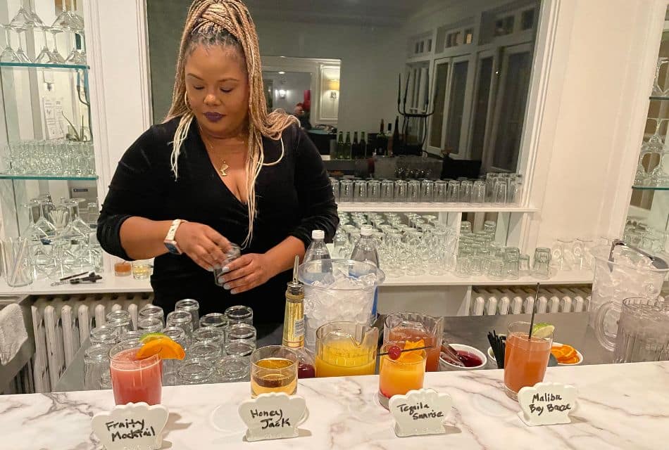 A woman in a black shirt behind a counter creating different types of colorful cocktails for a party