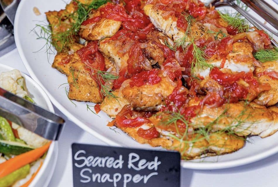 A white oval plate of food with a black sign with the words Seared Red Snapper