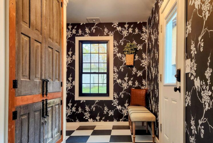 Foyer of a home with bold black and white floral wallpaper, checkered floor and sitting bench