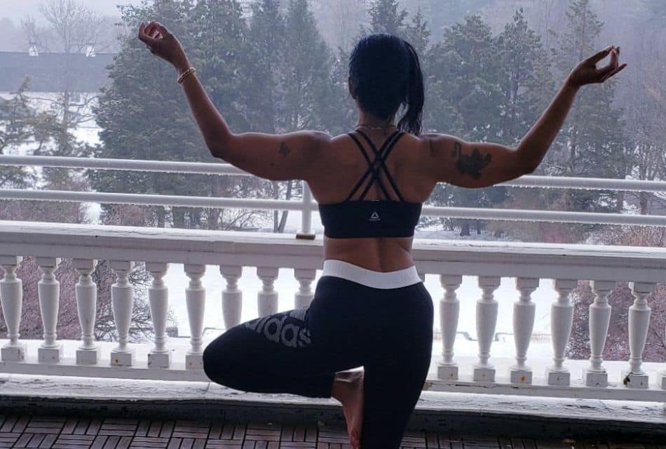 A woman in black and white workout clothes holding a yoga pose on an outdoor balcoony