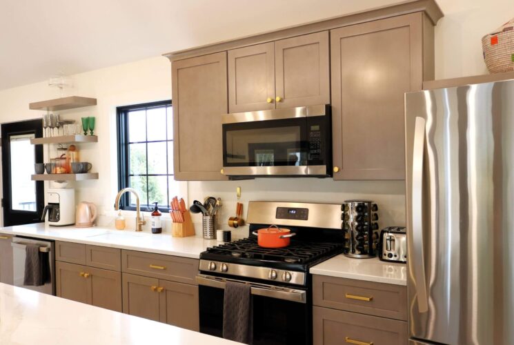 Bright kitchen with modern cabinets, floating shelves, stainless steel appliances and large paned window