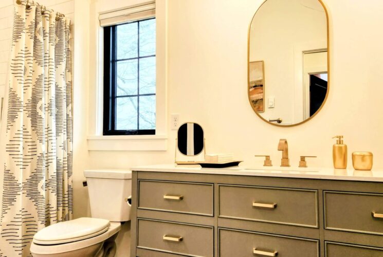 Elegant modern bathroom with vanity, gold faucet, gold rimmed oval mirror and black and white shower curtain