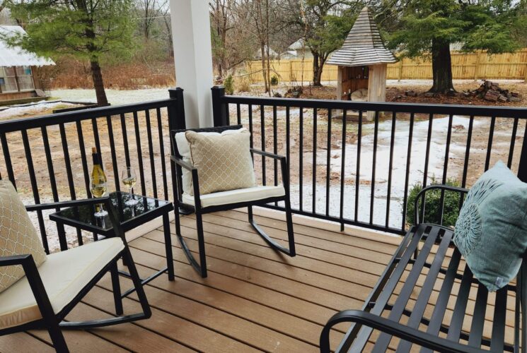 Outdoor patio with bench, two chairs and table to bottle of wine and two glasses