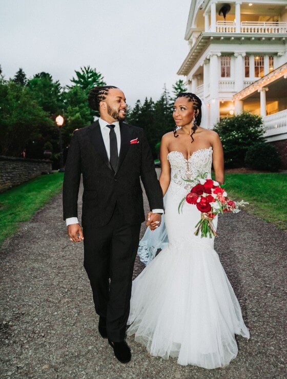 A bride and groom walking hand in hand down a path outside of a large white home