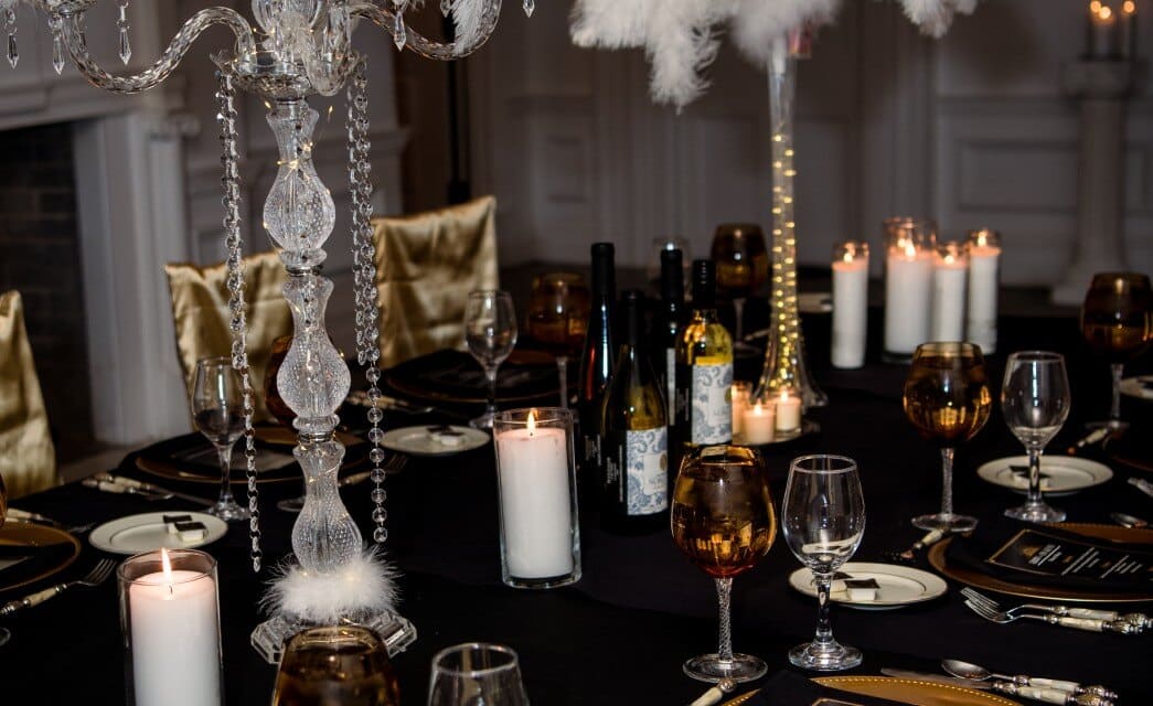 A dining table elegantly decorated with white candles, wine glasses and gold plates with black menus