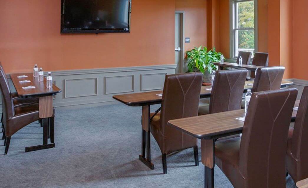 A business conference room with four sets of tables with leather chairs, TV hanging on a wall