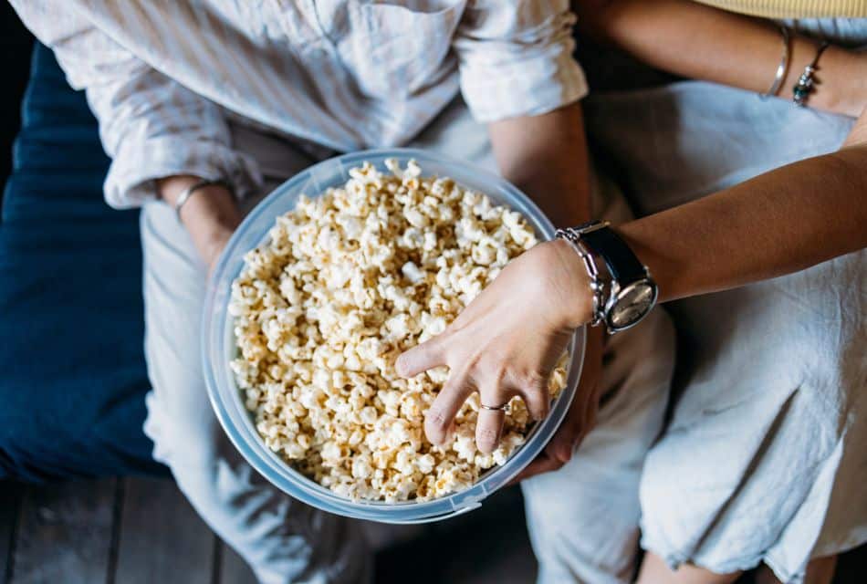 Two people sitting on a couch sharing a bowl of popcorn