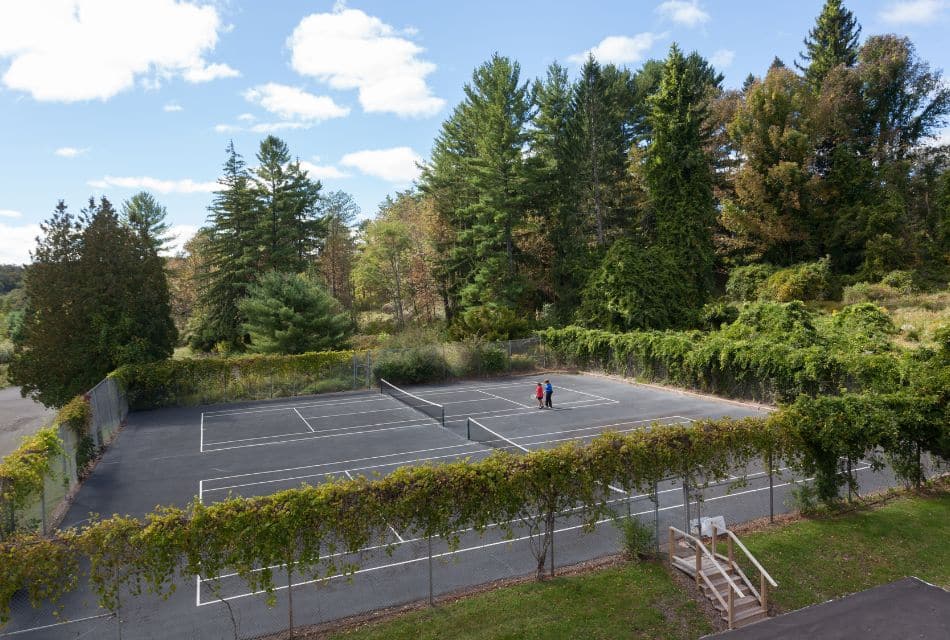 A large fenced tennis court surrounded by a forest of trees