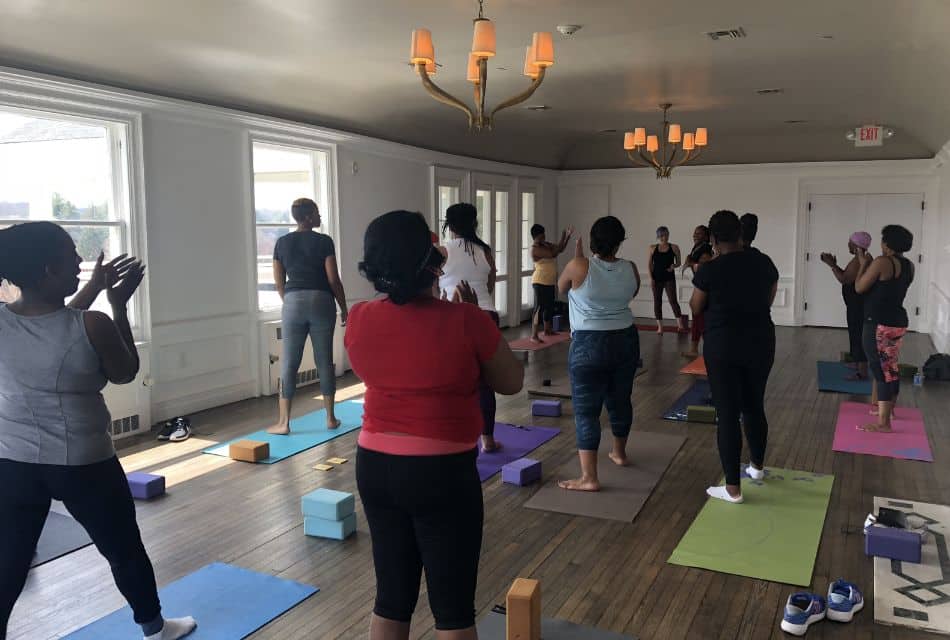 A large group of women in a studio with windows enjoying a yoga class together