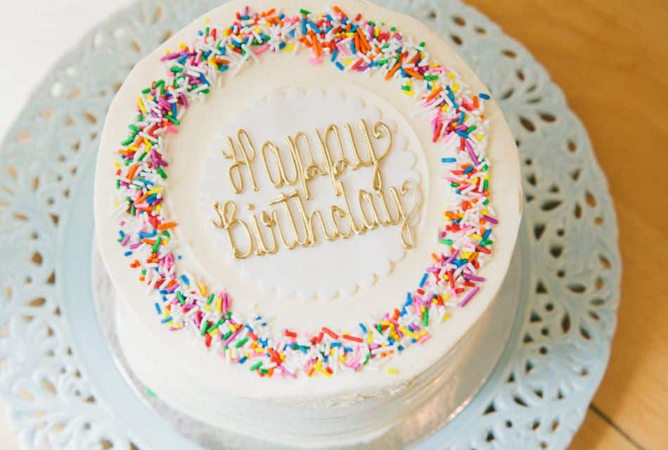 A round white birthday cake with multi colored sprinkles