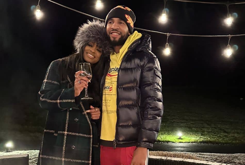 A man and woman standing outdoors by a fire put under a string of white lights