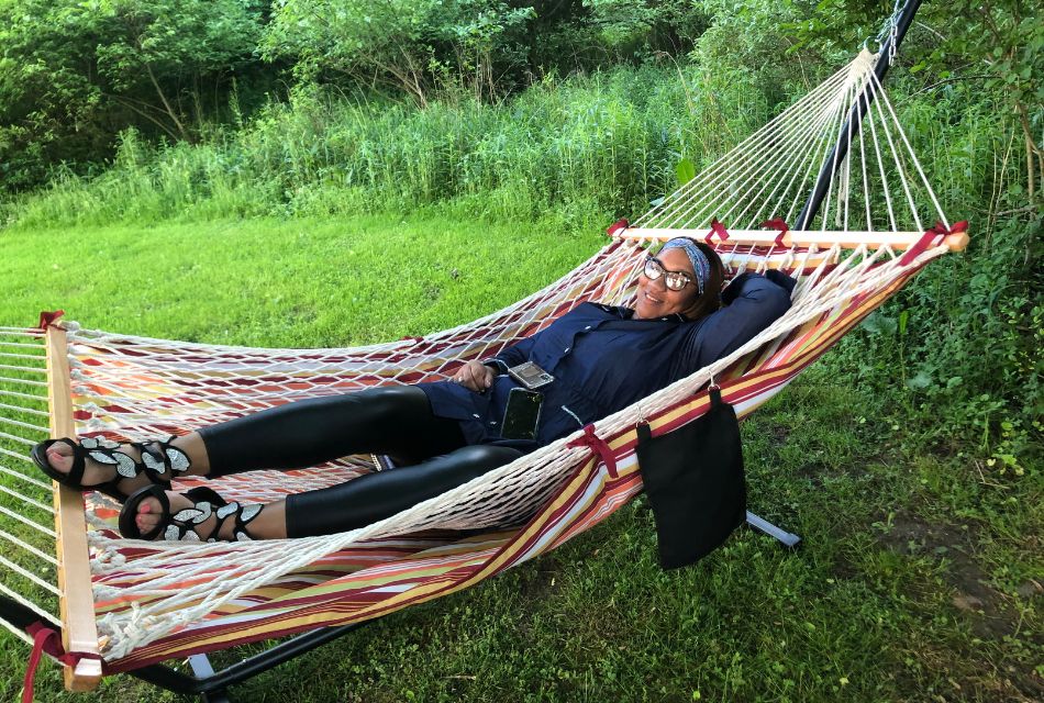 A woman laying in a striped hammock outside on a lawn surrounded by trees