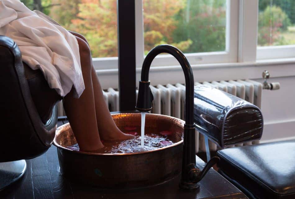 A woman sitting in a pedicure chair with her feet in a copper tub of water