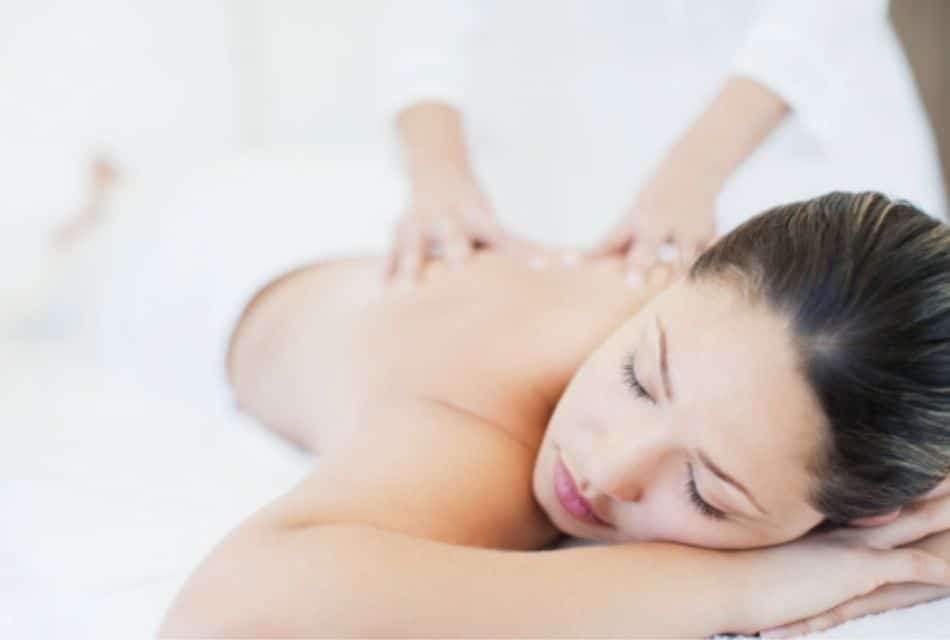 A woman laying on her stomach, covered with a white towel and a person massaging her back