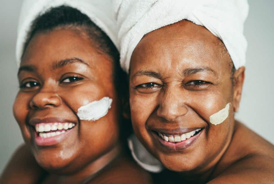 Two women smiling with white towels on their heads and white cream smeared across their cheeks