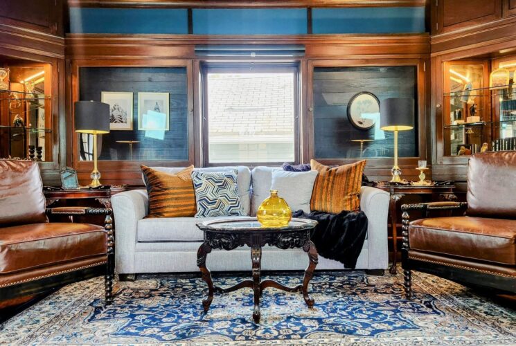 Elegant living room with dark wood detail, couch, leather chairs, oriental rug, and glass wall cabinets