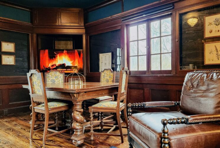 Sitting area with a unique corner gas fireplace, wood table with four chairs by a bright window and plush leather chair