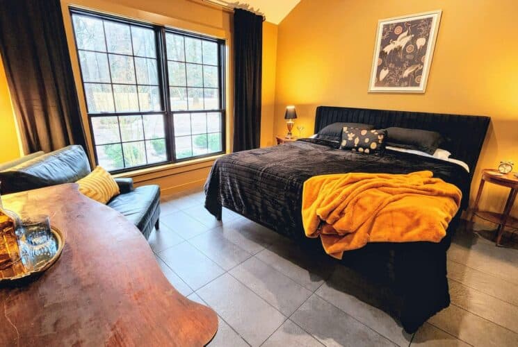 Spacious bedroom in hues of black and yellow, king bed, leather chair, large window with black curtains and wood table