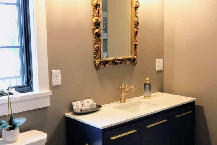 Elegant bathroom with dark wood vanity, gold faucet, ornate gold framed mirror and large window above the toilet