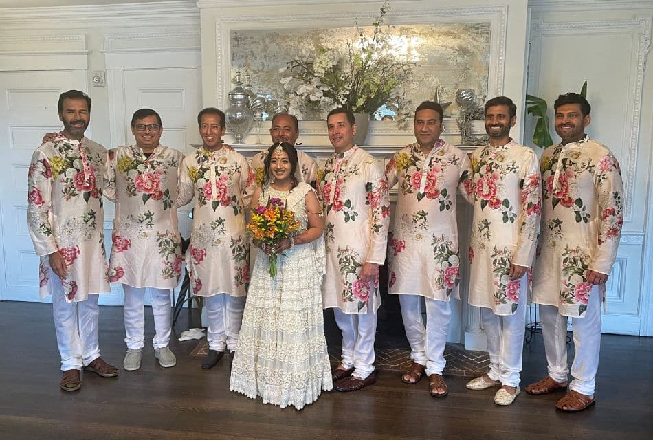A bride and groom with seven groomsmen, each wearing a colorful floral shirt with white pants